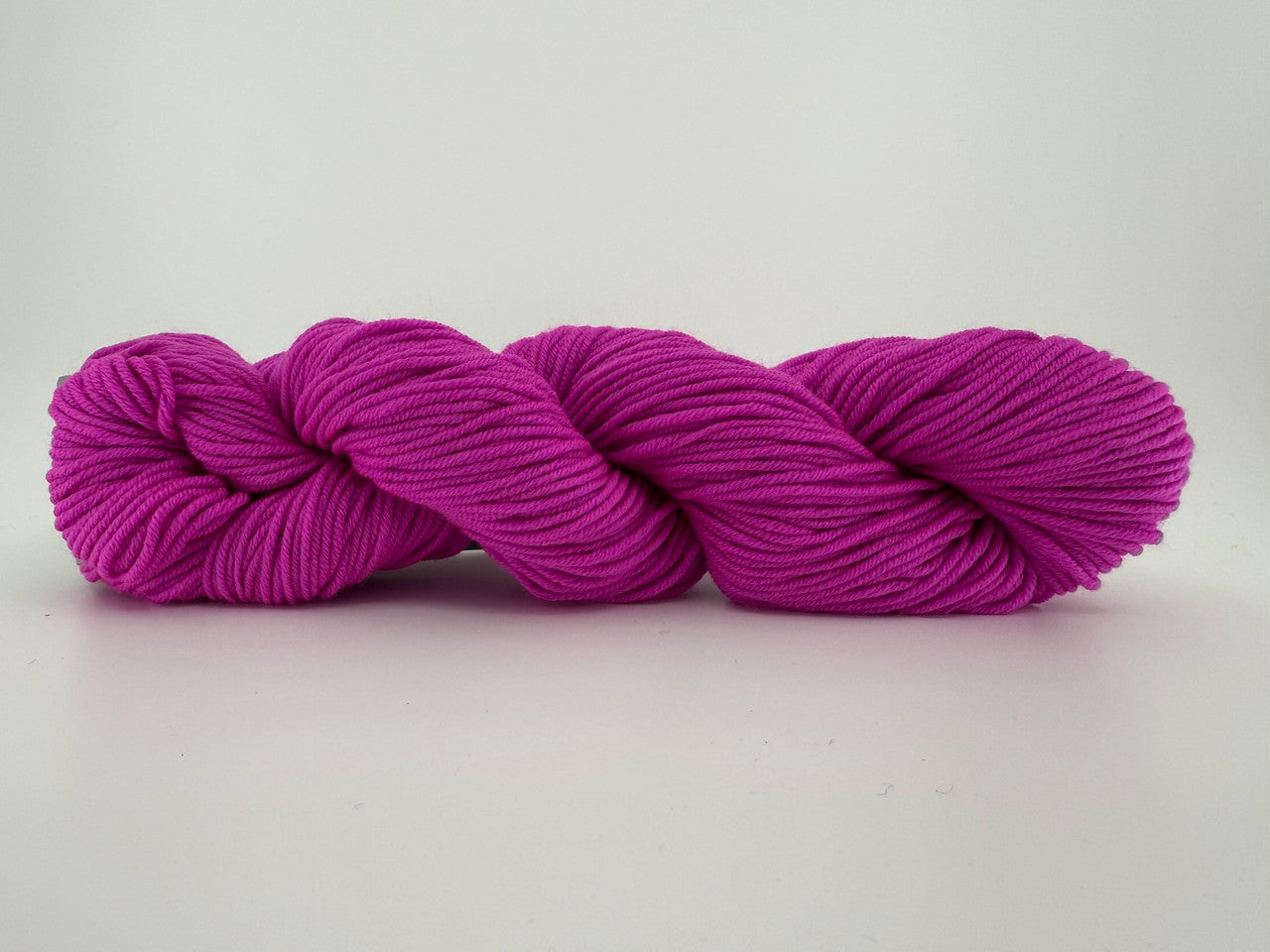 A skein of Plymouth DK Merino Superwash yarn in color Hot Pink
